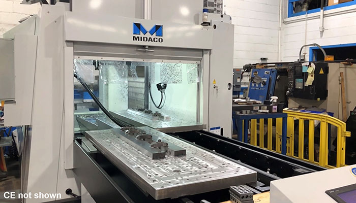 MIDACO Automatic Pallet Changer shuttle with metal parts on rectangle cast aluminum pallets. One pallet being transferred into the vertical machining center via the shuttle.