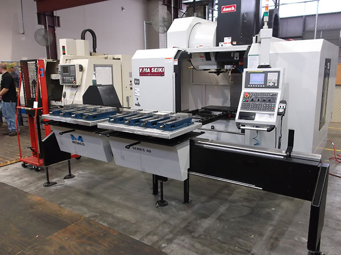 Midaco Manual Pallet Changer Shuttle with extended bridge in front of Vertical Machining Center in machine shop.